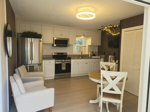 Een moderne keuken met witte kasten, roestvrijstalen apparatuur, een eethoek met een ronde tafel en stoelen, en een plafondlamp.