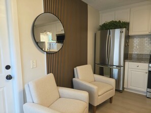 A modern kitchen with a stainless steel refrigerator, two beige armchairs, and a round mirror on the wall. - Family Nest Romantic Stay-Memories (Bradenton)