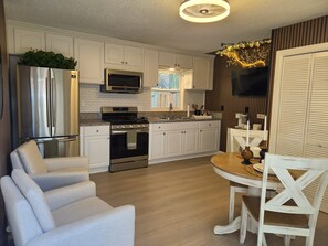 A modern kitchen with white cabinetry, stainless steel appliances, and a dining area with white chairs and a wooden table. - Family Nest Romantic Stay-Memories (Bradenton)