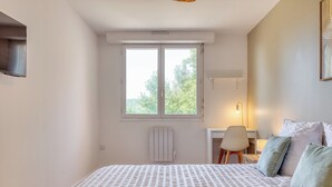A bedroom with a bed, a desk, and a chair. There is a window with a view of trees. - Le Devillois - 4 chambres, balcon et garage près de Rouen (Déville-lès-Rouen)