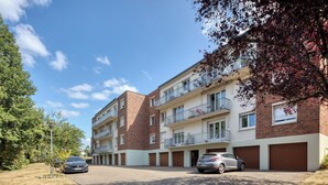 A multi-story residential building with a brick facade, balconies, and a parking area with cars. - Le Devillois - 4 chambres, balcon et garage près de Rouen (Déville-lès-Rouen)