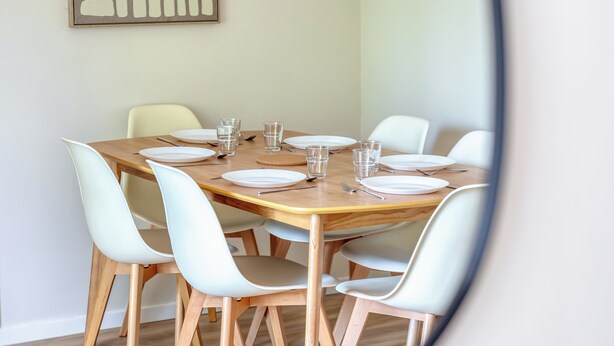 A dining area with a wooden table set for six, surrounded by white chairs. - Le Devillois - 4 chambres, balcon et garage près de Rouen (Déville-lès-Rouen)