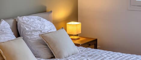 A neatly made bed with white linens and pillows, a bedside lamp, and a nightstand.