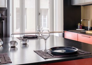 A modern kitchen with a dining area, featuring a black countertop, a glass bowl, wine glasses, and a water glass. - Valeria - Souplex élégant avec parking proche gare Rouen (Rouen)