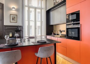 A modern kitchen with a central island, a built-in oven, and a window providing natural light. - Valeria - Souplex élégant avec parking proche gare Rouen (Rouen)