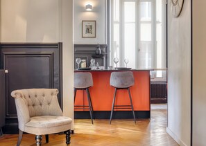 A room with a tufted armchair, a bar area with stools, and a large window. - Valeria - Souplex élégant avec parking proche gare Rouen (Rouen)