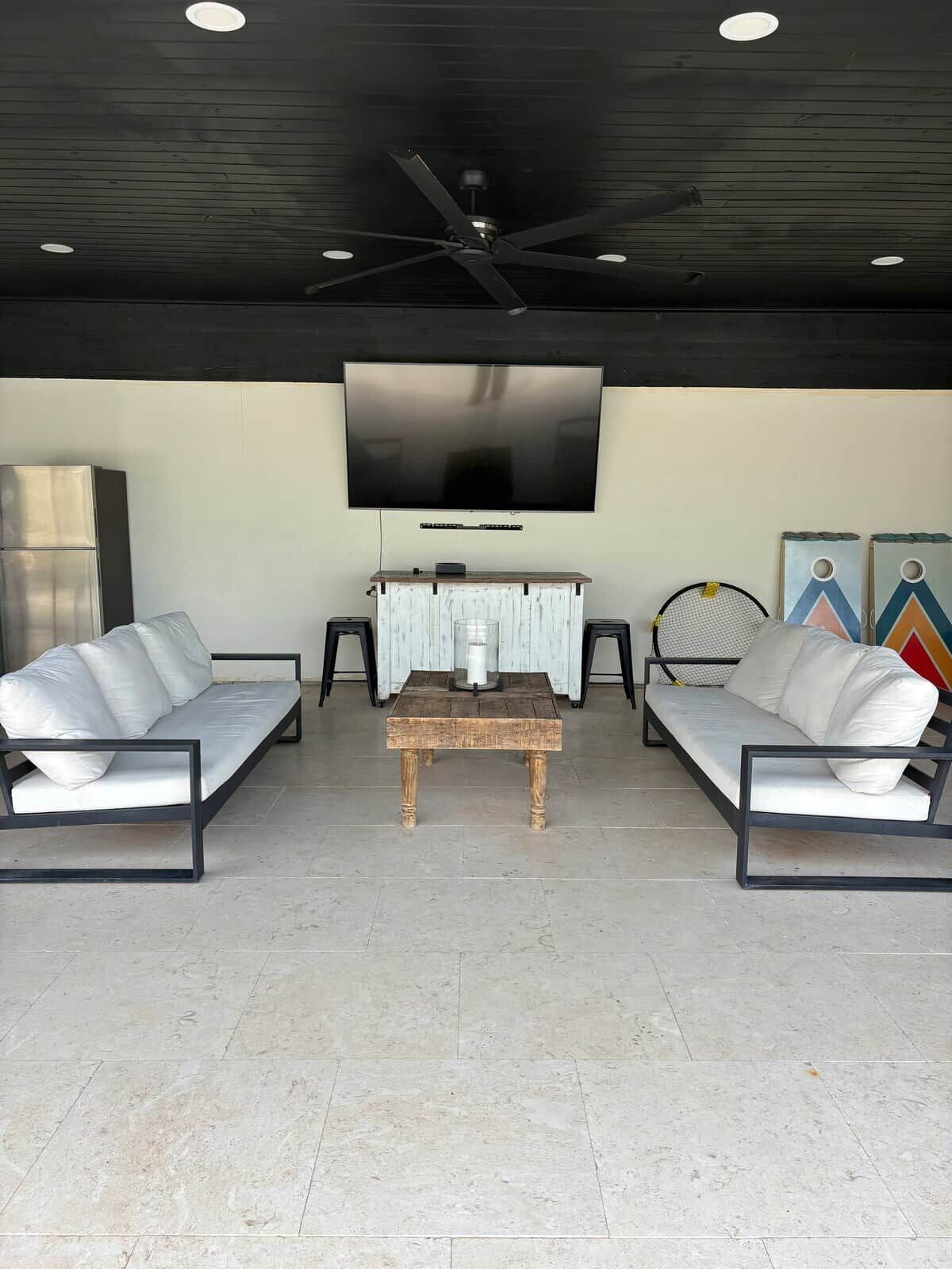 Uma sala de estar moderna com televisão de tela plana, dois sofás, uma mesa de centro e um ventilador de teto.