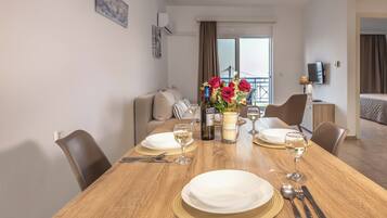 Uma sala de jantar com mesa de madeira posta para dois, pratos brancos, copos de vinho e uma garrafa de vinho.
