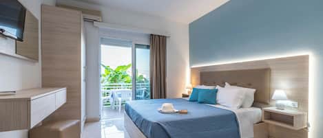 A hotel room with a bed, bedside table, lamp, and a view of the outdoors.