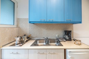 A kitchen with blue cabinets, a coffee maker, a kettle, and a jar on the counter.