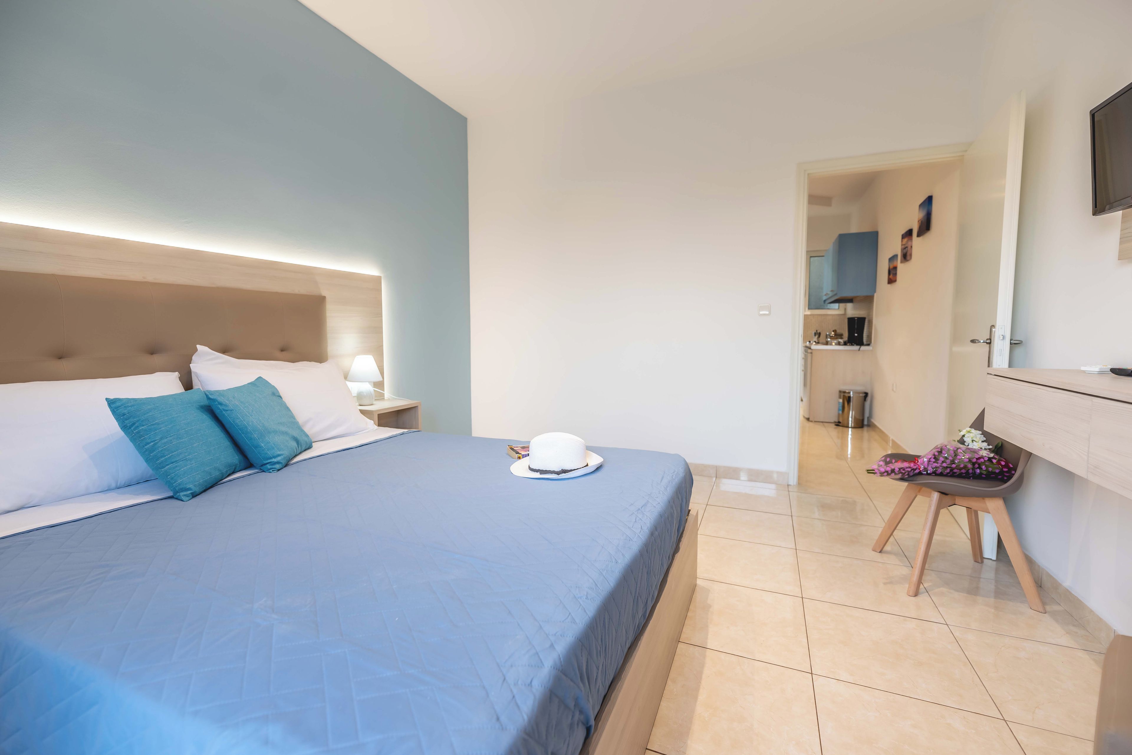 A hotel room with a bed, a nightstand, a desk, and a view into the kitchen.