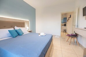 A hotel room with a bed, a nightstand, a desk, and a view into the kitchen.