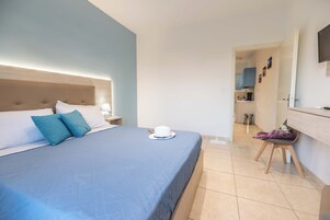 Habitación de hotel con una cama, una mesita de noche, un escritorio y vista a la cocina.