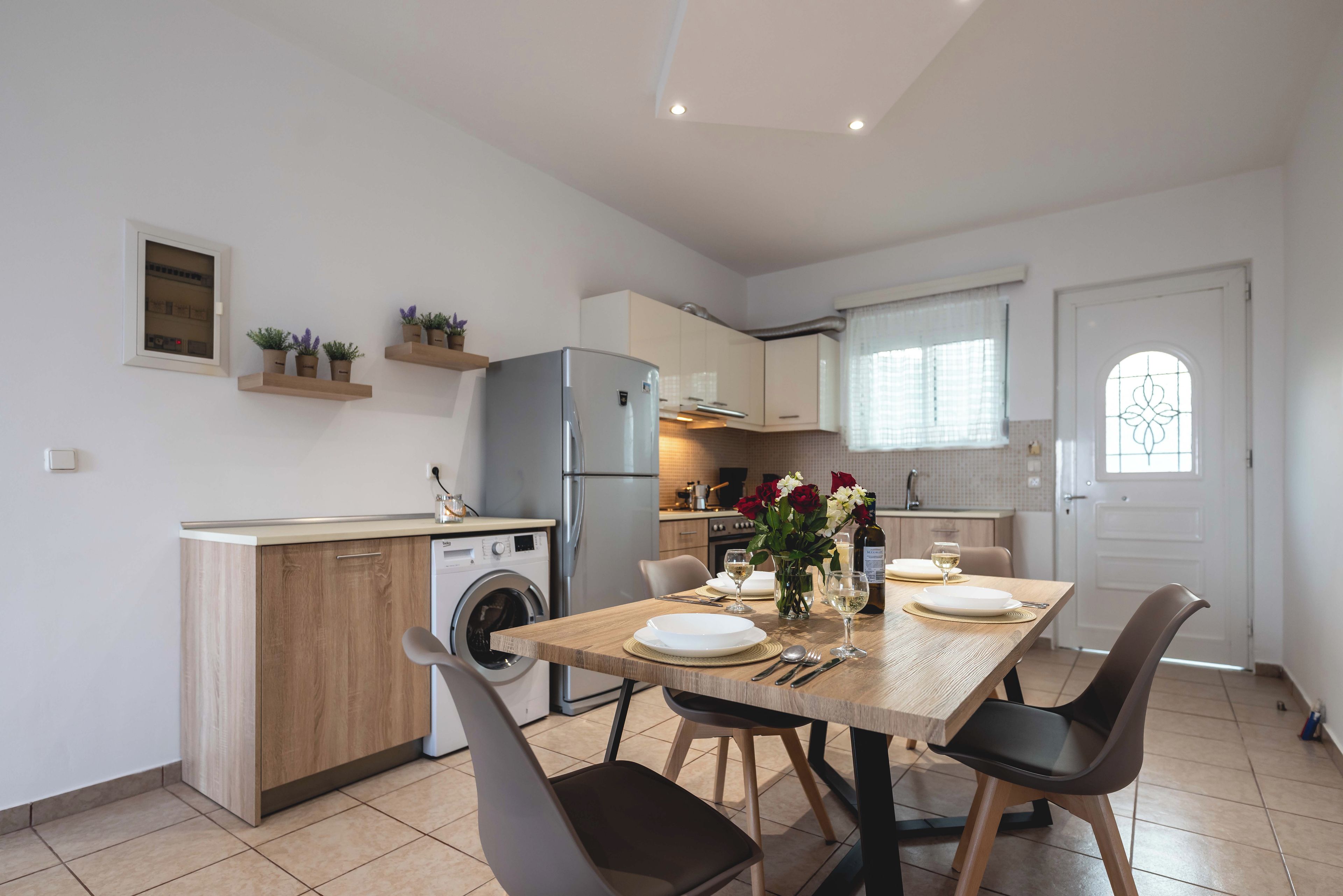 Cocina compacta con lavadora integrada, refrigerador y comedor con mesa lista para dos.
