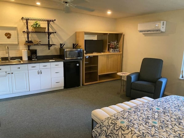 A compact room with a kitchenette, a bed, a chair, and a small table.