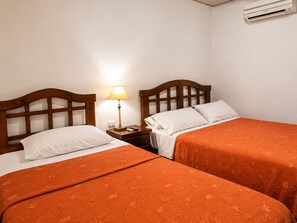 Habitación de hotel con dos camas, cada una con cabecero de madera, una mesita de noche con lámpara y un equipo de aire acondicionado en la pared.