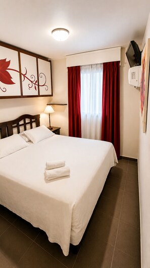 A hotel room with a large bed, a bedside table with a lamp, a window with red curtains, and a wall-mounted air conditioner. - HOTEL LAERTE (Mendoza)