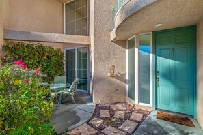 A modern building with a teal door, a glass door leading to a patio, and a small garden area with a glass table and chairs. - Skinny Dippin 2 Bedroom Townhouse (Palm Springs)