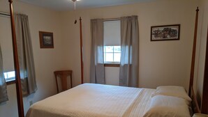 Una cama con dosel con colcha acolchada, una silla de madera, una ventana con cortinas y un cuadro en la pared.