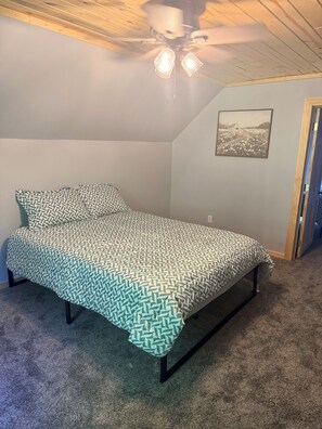 Ein Schlafzimmer mit einem Bett, einem Deckenventilator, einem an der Wand befestigten Bild und einem Teppichboden.