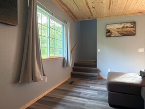 A room with a wooden staircase, a grey sofa, and a window with curtains.