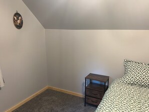 Ein Schlafzimmer mit einem Bett, einem Nachttisch, einer Kommode, einem Teppichboden und einem an der Wand hängenden Bild.