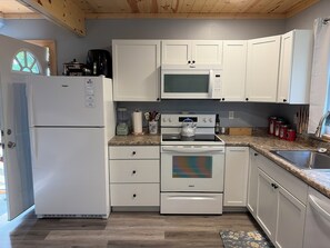 A modern kitchen with white appliances, including a refrigerator, microwave, and oven, with a granite countertop and wooden flooring. - Serene 3-bedroom house with AC just outside of Ladysmith. Pet-Friendly. (Ladysmith)