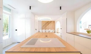 A modern kitchen with a central island, white cabinetry, and a view of a dining area with a wooden wall and white chairs. - POOL FRENCH VILLA WITH GYM , SAUNA - IN THE HEART OF CANNES- 250 SQM (Cannes)