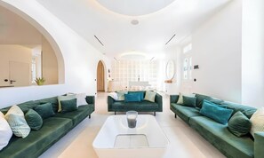 En moderne stue med to grønne sofaer, et hvidt sofabord og et køkkenområde i baggrunden.