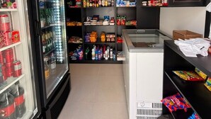 A store interior with shelves stocked with snacks and beverages, a refrigerated display case, and a freezer. - Pertinho do Mar, Brisa da Praia e 2 Quartos (Fortaleza)