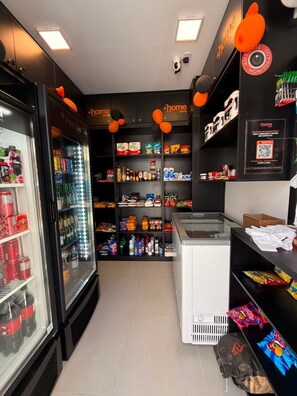 A store interior with shelves stocked with snacks and beverages, a refrigerated display case, and a freezer. - Pertinho do Mar, Brisa da Praia e 2 Quartos (Fortaleza)