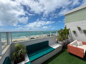 A balcony with a view of the beach, a green sofa, and potted plants. - Pertinho do Mar, Brisa da Praia e 2 Quartos (Fortaleza)