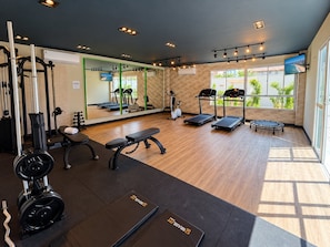 Ein Fitnessraum mit Trainingsgeräten, einem Spiegel und einem Fenster mit Blick auf Palmen.