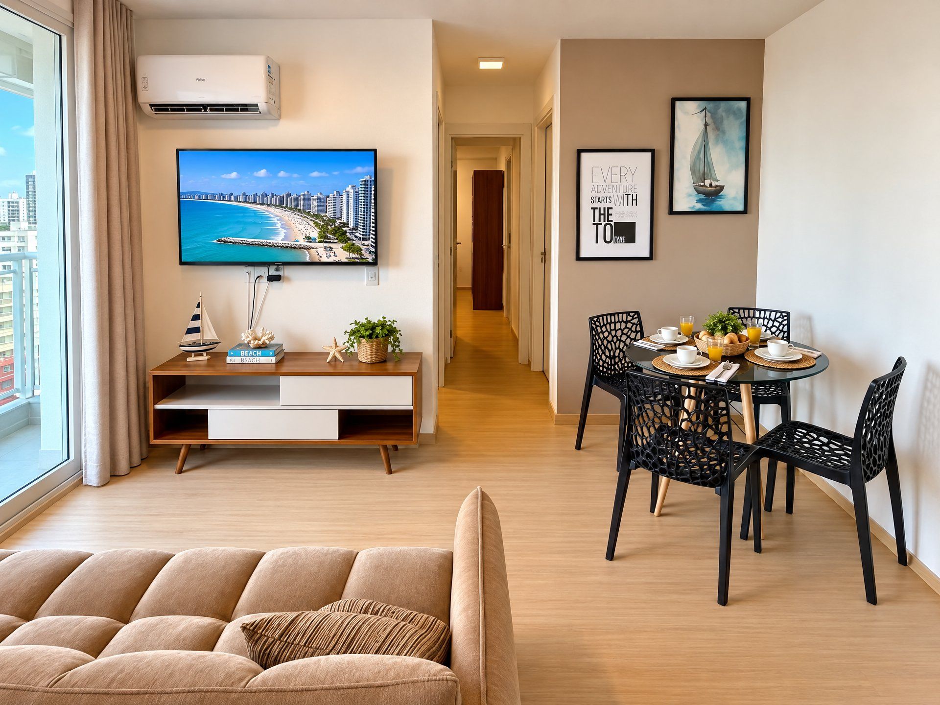 Una sala moderna con un sofá, una zona de comedor con mesa y sillas, un televisor mostrando una escena de playa y un pasillo que conduce a un baño.
