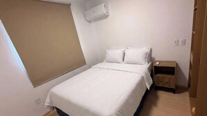 A bedroom with a bed, a bedside table, a wardrobe, and a window with a blind. - Pertinho do Mar, Brisa da Praia e 2 Quartos (Fortaleza)