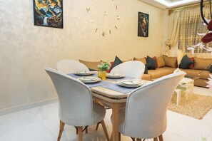A dining area with a table set for four, a sofa in the background, and a clock on the wall. - Tanger Élégance Smart Stay WIFI & Netflix (Tanger)