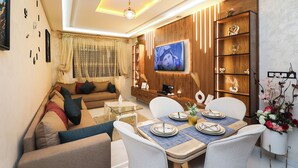 Ein modernes Wohnzimmer mit Sofa, Fernseher, Esstisch und dekorativen Regalen.