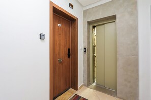 A wooden door with a number plate, a modern elevator, and a small rug on the floor. - Tanger Élégance Smart Stay WIFI & Netflix (Tanger)