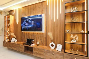 A modern living room with a wooden TV stand, a flat-screen TV displaying a movie, and a decorative shelf with heart-shaped items. - Tanger Élégance Smart Stay WIFI & Netflix (Tanger)
