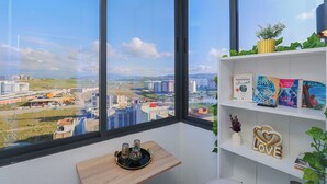 Ein Zimmer mit großem Fenster, einem hölzernen Regal mit Büchern, einem dekorativen Schild und einem kleinen Tisch mit Tablett.