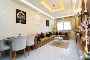 A modern living room with a sofa, chairs, a coffee table, a clock, and artwork on the wall. - Tanger Élégance Smart Stay WIFI & Netflix (Tanger)
