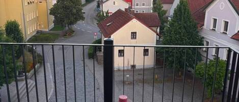 Un balcón con dos sillas y una mesa, con vista a una calle con edificios y árboles.