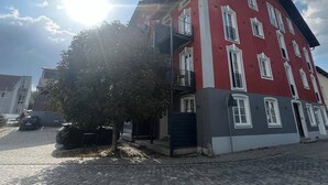 A red building with multiple windows and balconies, situated on a cobblestone street. - Eibisch Apartments (Passau)