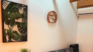 A modern living room with a grey sofa, a small side table with a plant, a framed artwork, and a wooden beam ceiling. - Eibisch Apartments (Passau)