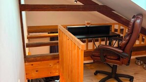 A loft bedroom with exposed wooden beams, a desk, a chair, and a small seating area with cushions. - Eibisch Apartments (Passau)