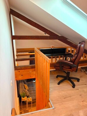 Een slaapkamer in loftstijl met zichtbare houten balken, een bureau, een stoel en een zithoek met kussens.