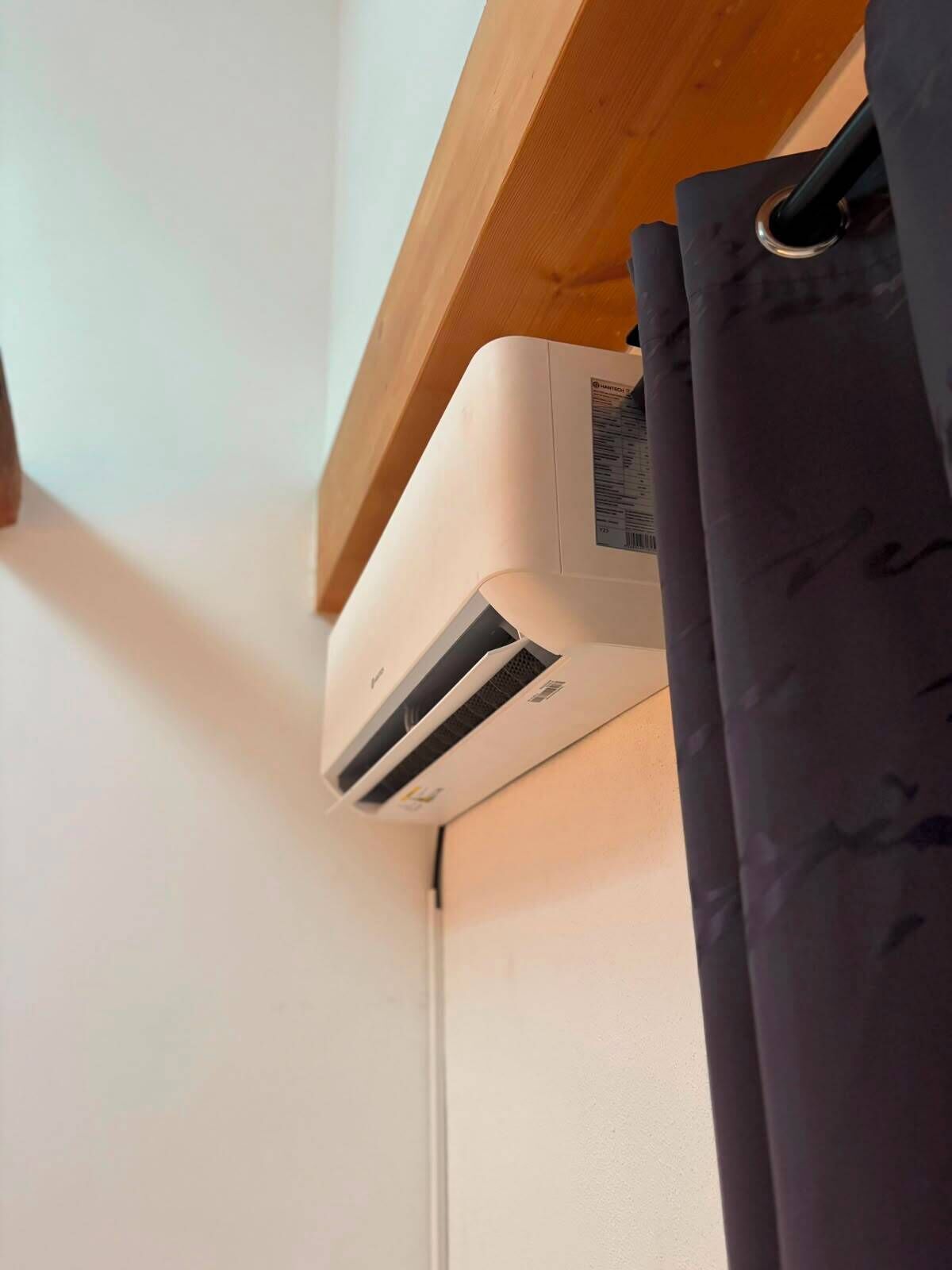 A white air conditioning unit mounted on a wall with a wooden beam above it.