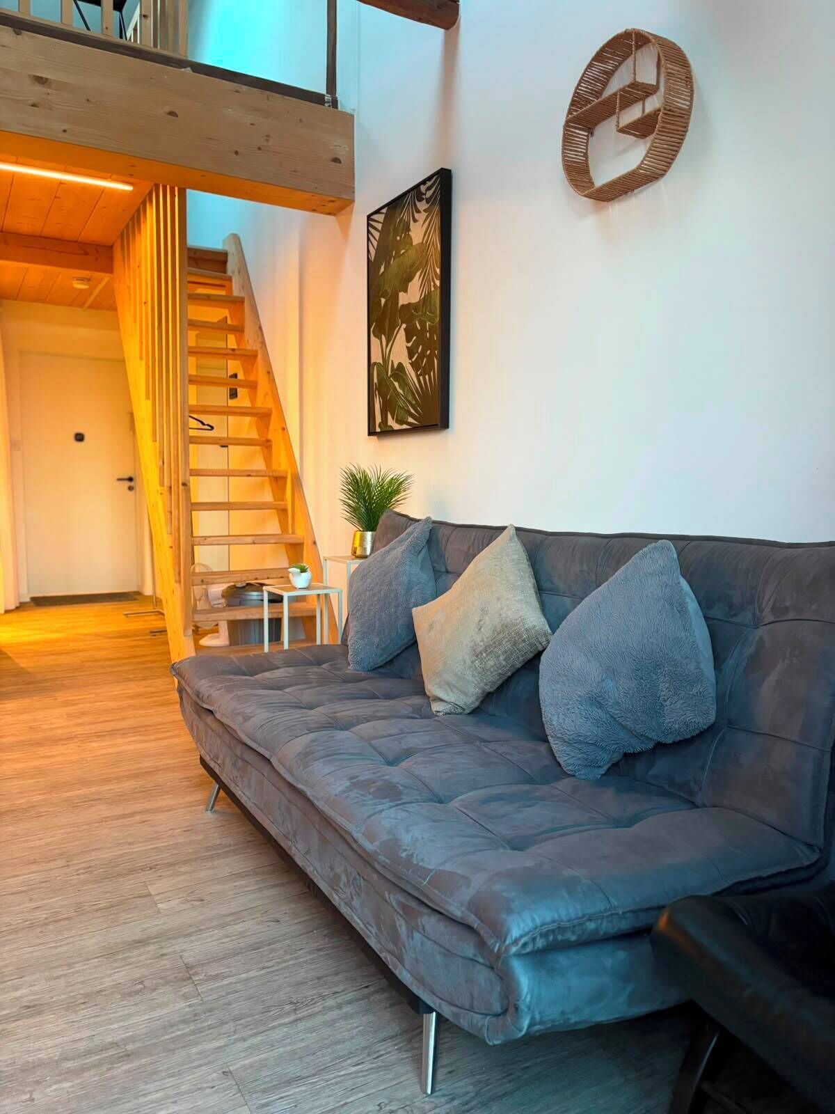 A modern living room with a grey sofa, a wooden staircase, and a wall-mounted artwork.