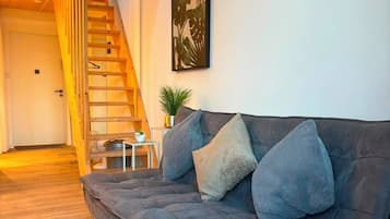 A modern living room with a grey sofa, a wooden staircase, and a wall-mounted artwork.