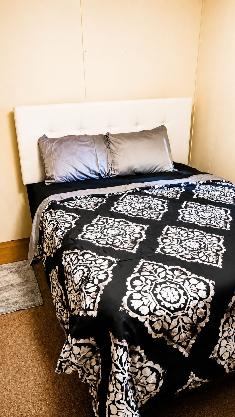 A bed with a white headboard, a black and white patterned bedspread, and a grey pillow.